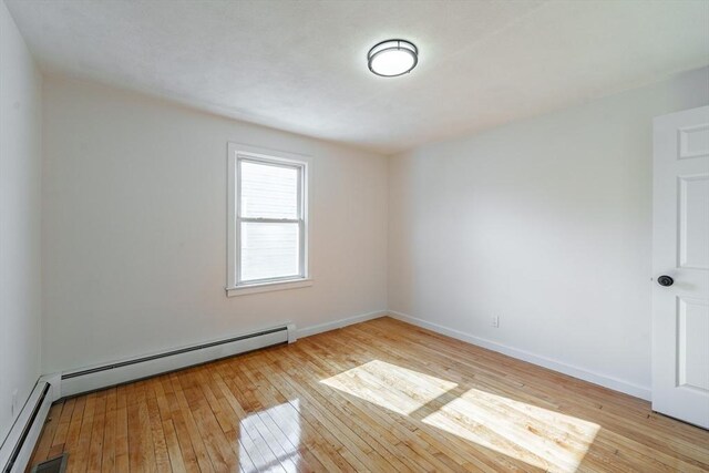 empty room with light wood finished floors, a baseboard radiator, visible vents, and baseboards