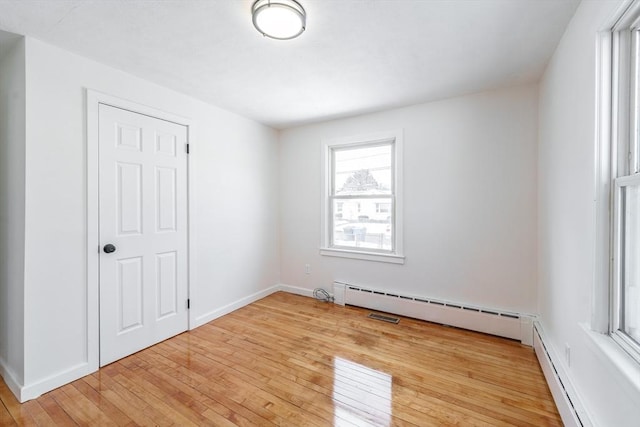 spare room featuring light wood-type flooring, a baseboard radiator, and baseboards