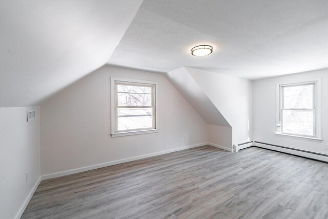 bonus room featuring lofted ceiling, light wood finished floors, baseboard heating, and baseboards