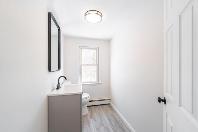 bathroom with toilet, a baseboard heating unit, vanity, wood finished floors, and baseboards