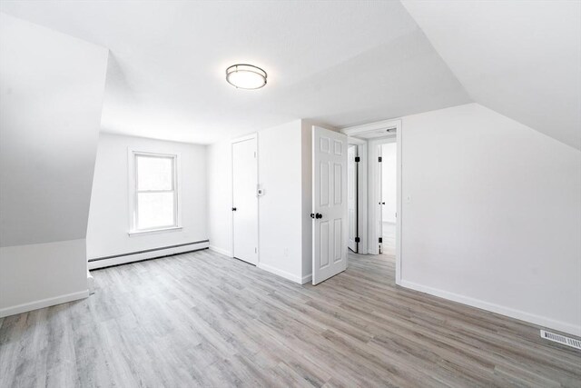 additional living space with lofted ceiling, a baseboard radiator, visible vents, baseboards, and light wood finished floors