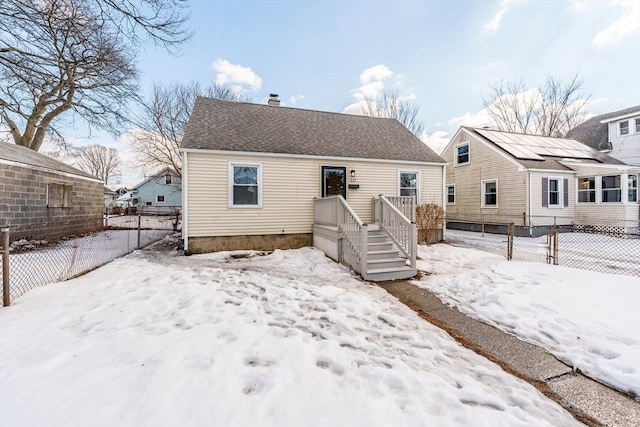 snow covered property with roof with shingles, a chimney, and fence