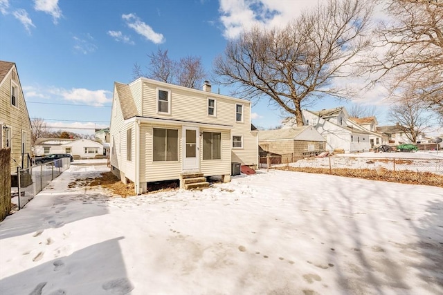 snow covered house with a chimney, central AC unit, entry steps, fence, and a residential view