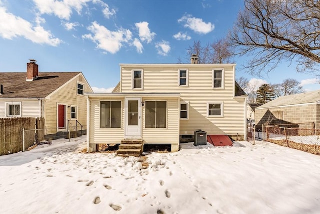 snow covered rear of property with entry steps, central air condition unit, and fence