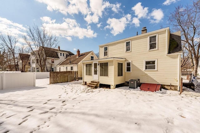 snow covered rear of property with entry steps, central AC unit, and fence