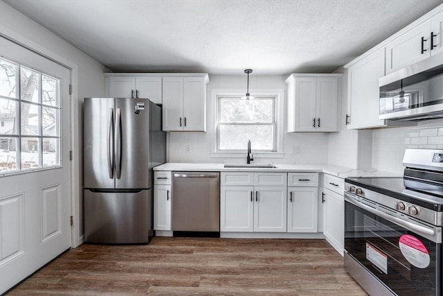 kitchen with hanging light fixtures, stainless steel appliances, light countertops, white cabinetry, and a sink