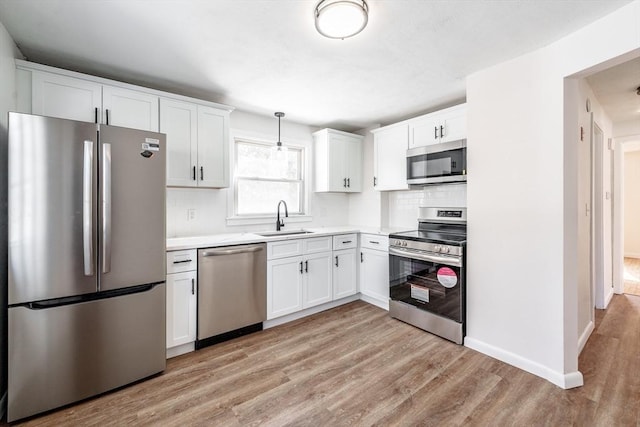 kitchen with decorative light fixtures, light countertops, appliances with stainless steel finishes, white cabinets, and a sink