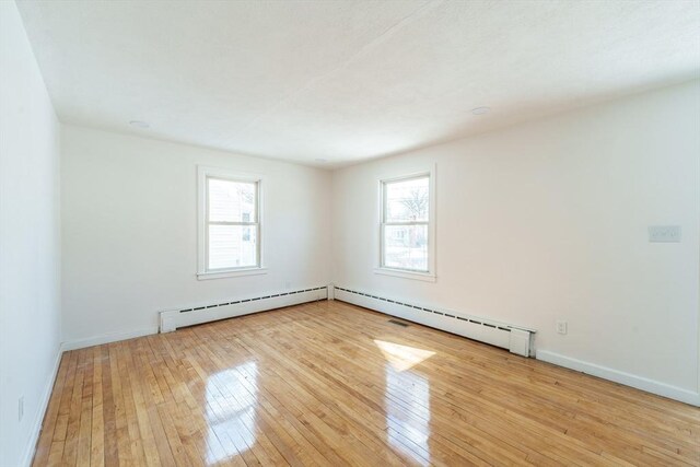 empty room featuring a baseboard radiator, light wood-style flooring, and baseboards