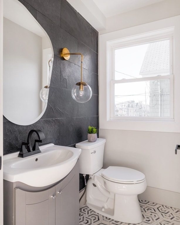 bathroom featuring tasteful backsplash, tile patterned flooring, toilet, vanity, and tile walls