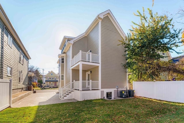 back of house featuring a yard, a balcony, central AC, and a patio area