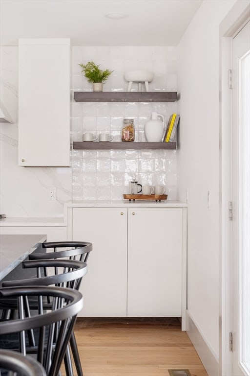 bar featuring white cabinets, light hardwood / wood-style floors, and tasteful backsplash