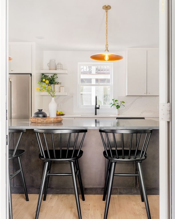 bar featuring stainless steel refrigerator, white cabinets, pendant lighting, and light wood-type flooring