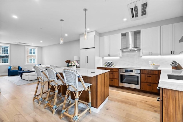 kitchen featuring wall chimney range hood, paneled built in refrigerator, visible vents, oven, and a kitchen breakfast bar