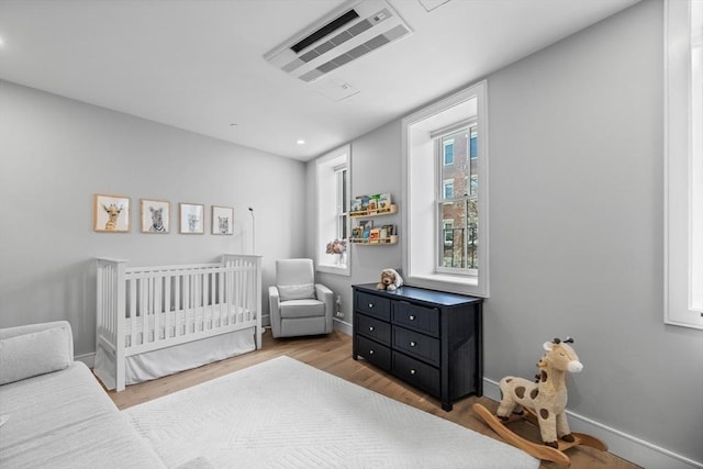 bedroom with visible vents, a crib, baseboards, and wood finished floors