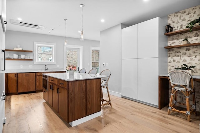 kitchen with open shelves, a breakfast bar area, light countertops, light wood-style flooring, and a sink