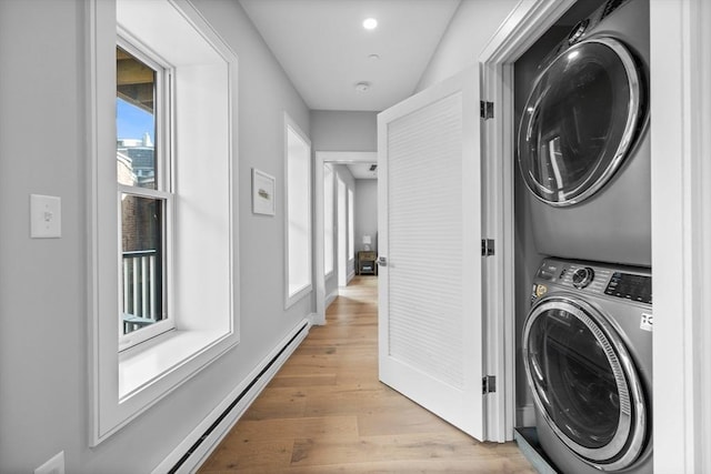 washroom with baseboards, laundry area, stacked washer and clothes dryer, a baseboard heating unit, and light wood-type flooring