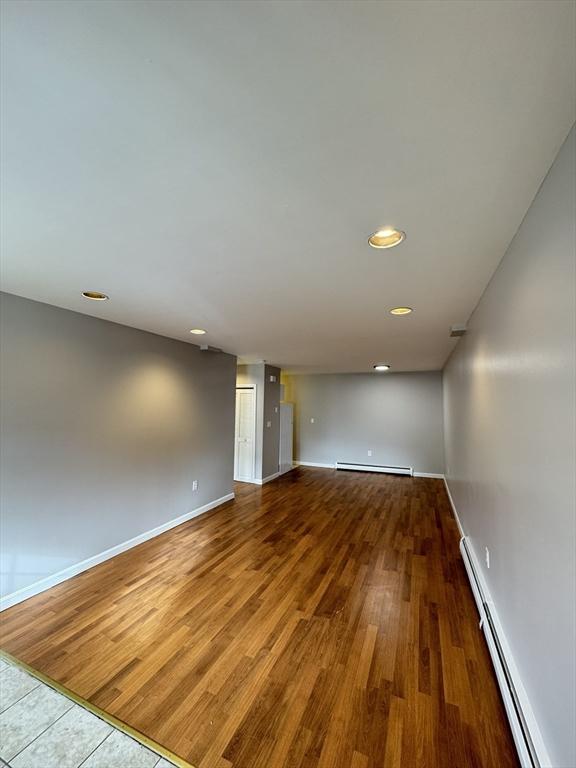 unfurnished room featuring recessed lighting, a baseboard radiator, wood finished floors, and baseboards