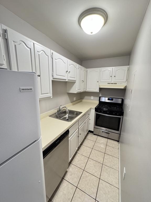 kitchen with light tile patterned floors, stainless steel appliances, a sink, white cabinetry, and light countertops