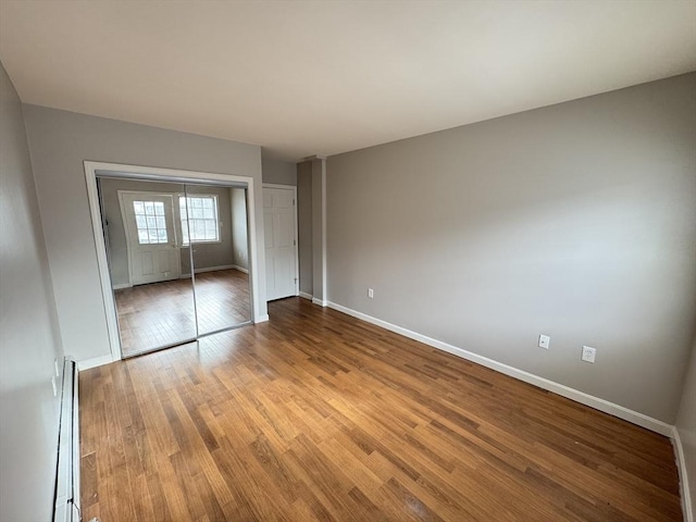 unfurnished bedroom featuring baseboards, a closet, a baseboard heating unit, and wood finished floors