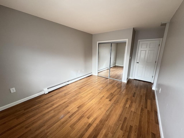 unfurnished bedroom featuring baseboards, dark wood finished floors, a baseboard radiator, baseboard heating, and a closet