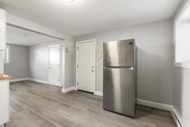 kitchen with freestanding refrigerator, a baseboard heating unit, light wood finished floors, and white cabinets