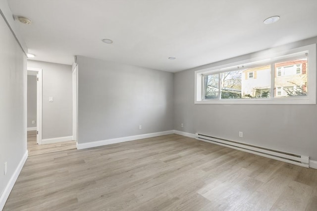 empty room with baseboard heating, light wood-style floors, baseboards, and a smoke detector