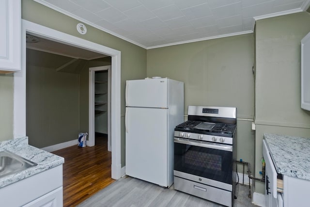 kitchen featuring white refrigerator, crown molding, light hardwood / wood-style flooring, gas stove, and white cabinetry