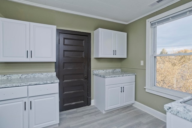 kitchen with white cabinets, a healthy amount of sunlight, light hardwood / wood-style floors, and ornamental molding