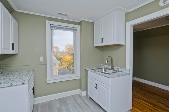 kitchen with white cabinets, ornamental molding, sink, and light hardwood / wood-style flooring