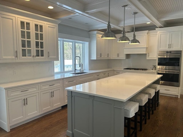 kitchen featuring beamed ceiling, white cabinetry, dark wood-style flooring, a sink, and stainless steel double oven