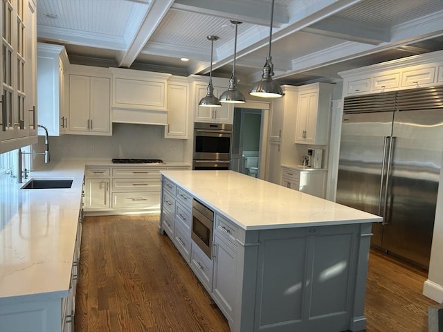 kitchen with beamed ceiling, white cabinets, built in appliances, and dark wood finished floors