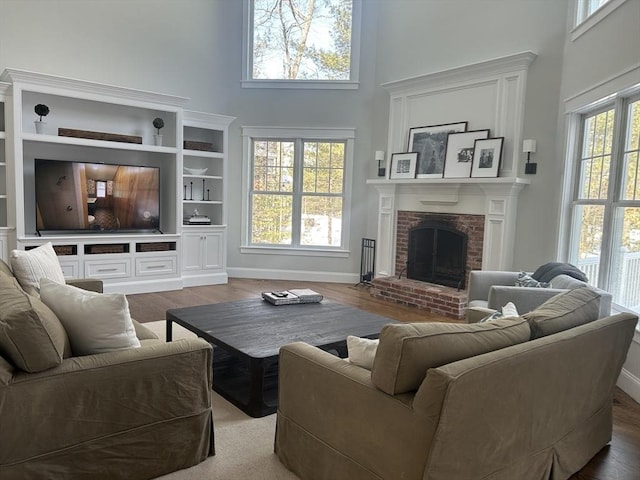 living area featuring a fireplace, a towering ceiling, baseboards, and wood finished floors