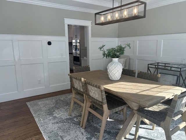 dining room featuring a notable chandelier, a decorative wall, ornamental molding, dark wood-type flooring, and a wainscoted wall
