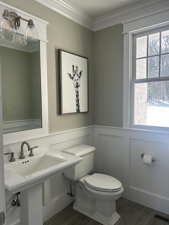 half bathroom with crown molding, a wainscoted wall, toilet, a decorative wall, and a sink