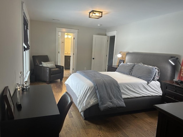 bedroom featuring wood finished floors, visible vents, and connected bathroom