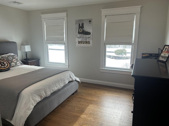 bedroom with wood finished floors, baseboards, multiple windows, and visible vents