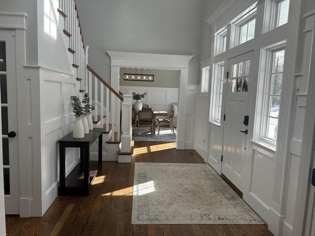 foyer with a decorative wall, stairway, wood finished floors, a high ceiling, and wainscoting