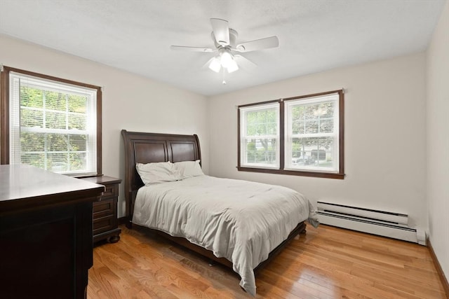 bedroom with a baseboard heating unit, multiple windows, light wood finished floors, and ceiling fan