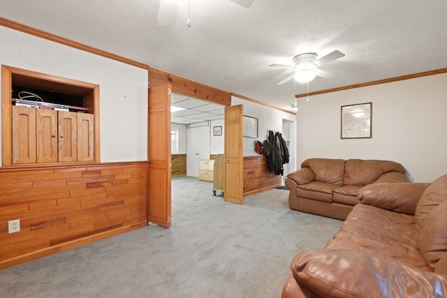 living room with a ceiling fan, crown molding, light colored carpet, wood walls, and a wainscoted wall