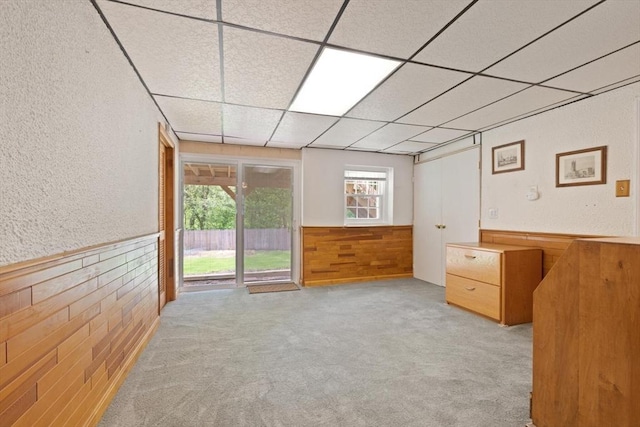 unfurnished room with wooden walls, a drop ceiling, a wainscoted wall, carpet, and a textured wall