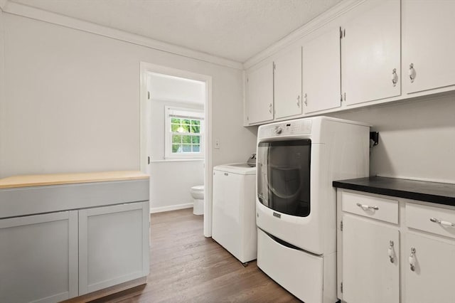 laundry room with cabinet space, washing machine and clothes dryer, wood finished floors, and crown molding