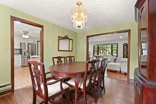 dining space with wood-type flooring, a baseboard heating unit, a chandelier, ceiling fan, and baseboards