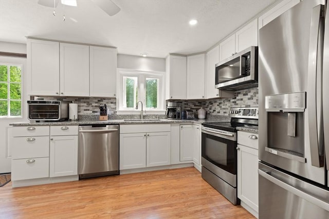 kitchen with appliances with stainless steel finishes, a sink, tasteful backsplash, dark stone counters, and recessed lighting