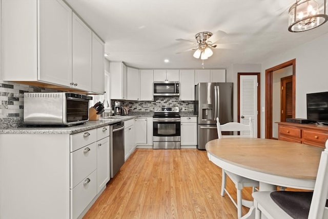 kitchen featuring stainless steel appliances, a ceiling fan, white cabinetry, tasteful backsplash, and light wood-style floors