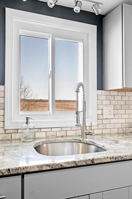 67 N End Blvd Unit 1, Salisbury, MA 01952 - kitchen view of a sink, white cabinets, light stone counters, and decorative backsplash