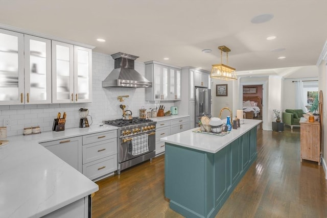 kitchen with wall chimney range hood, tasteful backsplash, decorative light fixtures, a center island with sink, and high end appliances