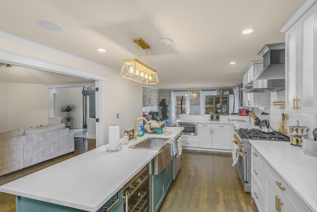 kitchen with a center island with sink, wall chimney range hood, high end stainless steel range oven, hanging light fixtures, and white cabinetry