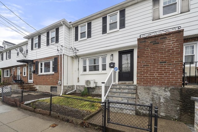 townhome / multi-family property featuring entry steps, brick siding, a gate, a fenced front yard, and ac unit