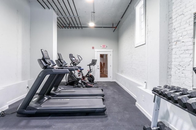 workout area featuring baseboards and brick wall