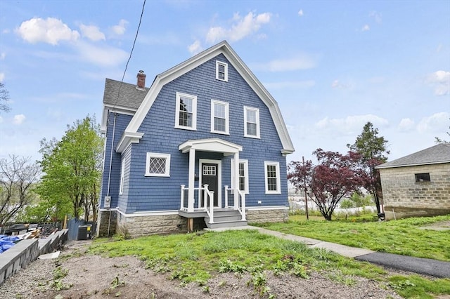 colonial inspired home featuring a gambrel roof, a chimney, and a front yard